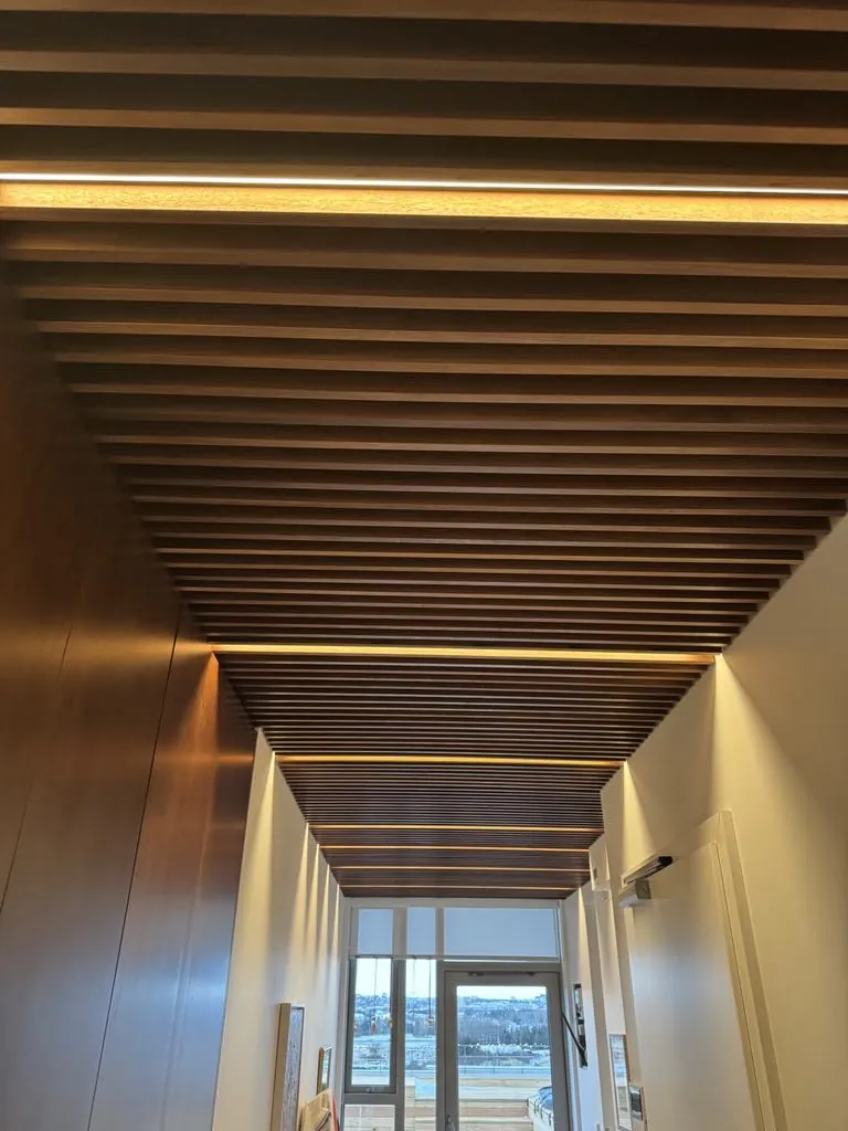 Corridor with indirect lighting in a timber-slat ceiling